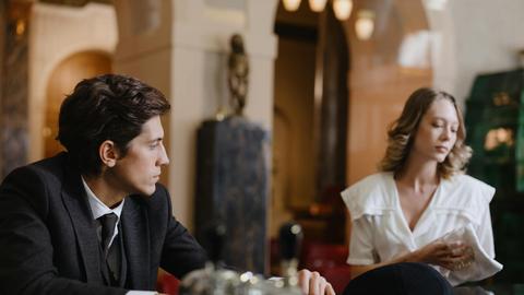 A man and woman engage in conversation at a classic, elegant hotel bar.
