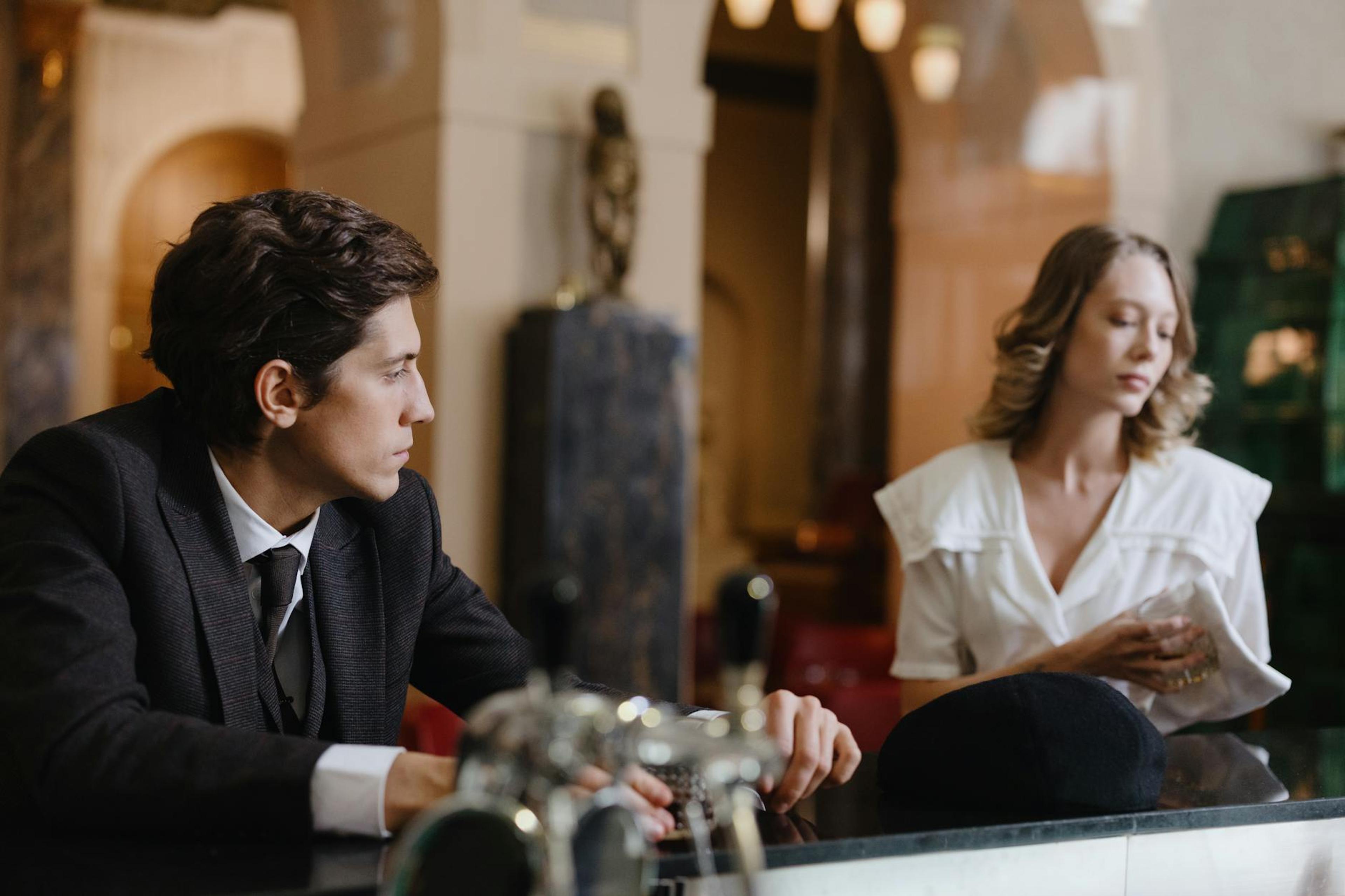 A man and woman engage in conversation at a classic, elegant hotel bar.