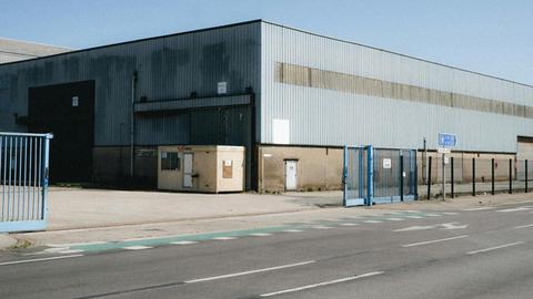 View of a large industrial warehouse in Dunkerque, showcasing its metal structure and broad entrance. Clear sky day.