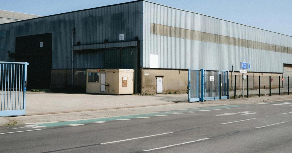 View of a large industrial warehouse in Dunkerque, showcasing its metal structure and broad entrance. Clear sky day.