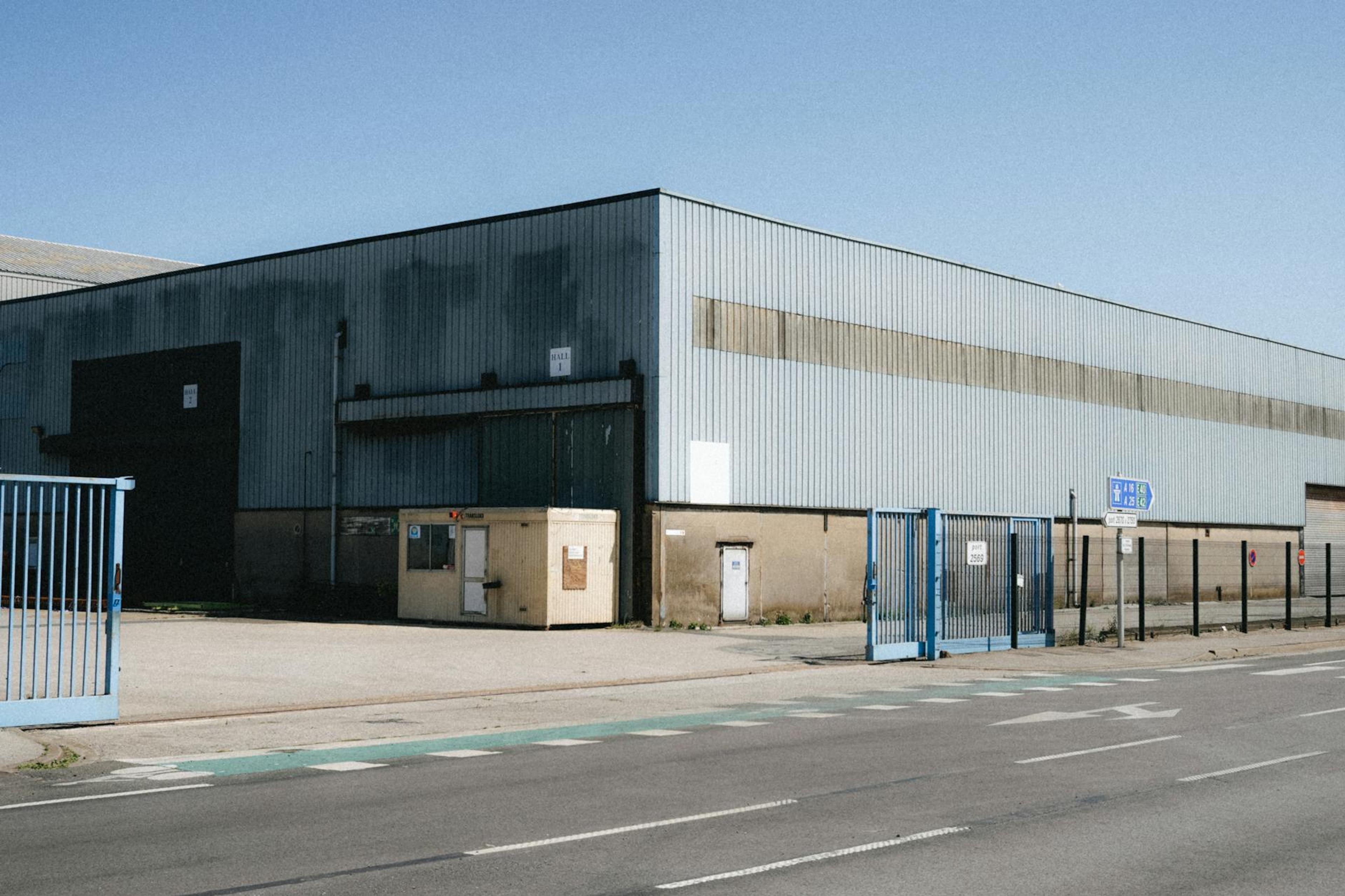 View of a large industrial warehouse in Dunkerque, showcasing its metal structure and broad entrance. Clear sky day.