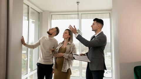 A young couple inspects a modern apartment with a real estate agent during a daytime viewing.