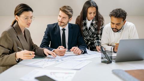 Diverse team discussing a business plan at an office desk with laptops and documents.