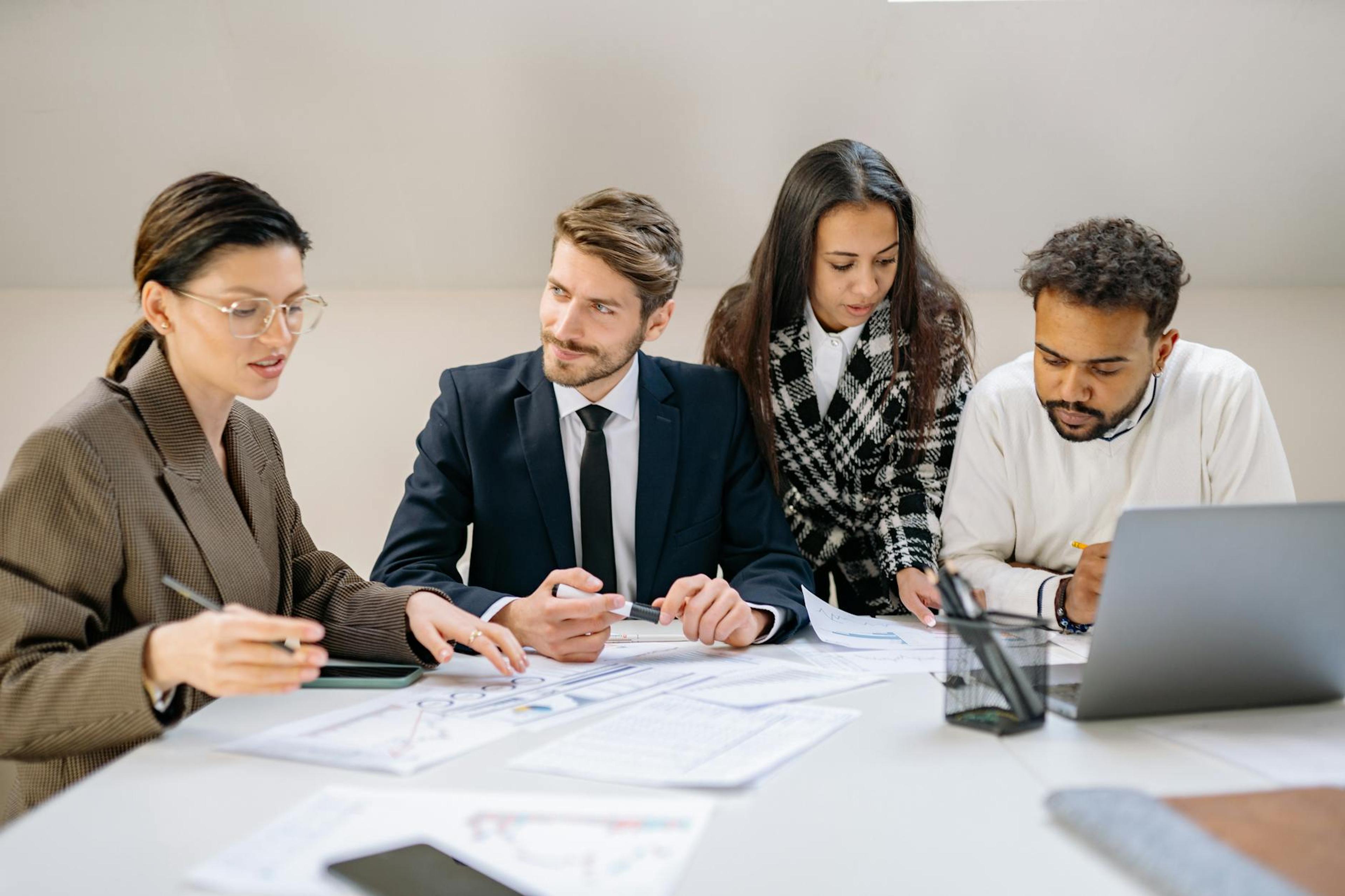 Diverse team discussing a business plan at an office desk with laptops and documents.