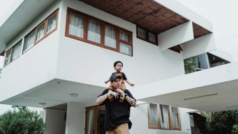 Father and son bonding on a piggyback ride in front of a modern house with unique architecture.