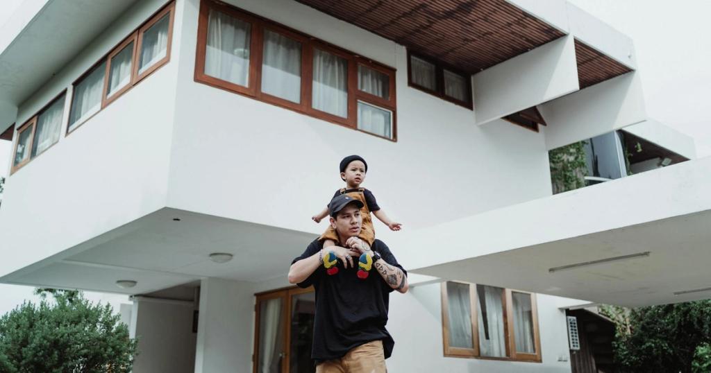 Father and son bonding on a piggyback ride in front of a modern house with unique architecture.