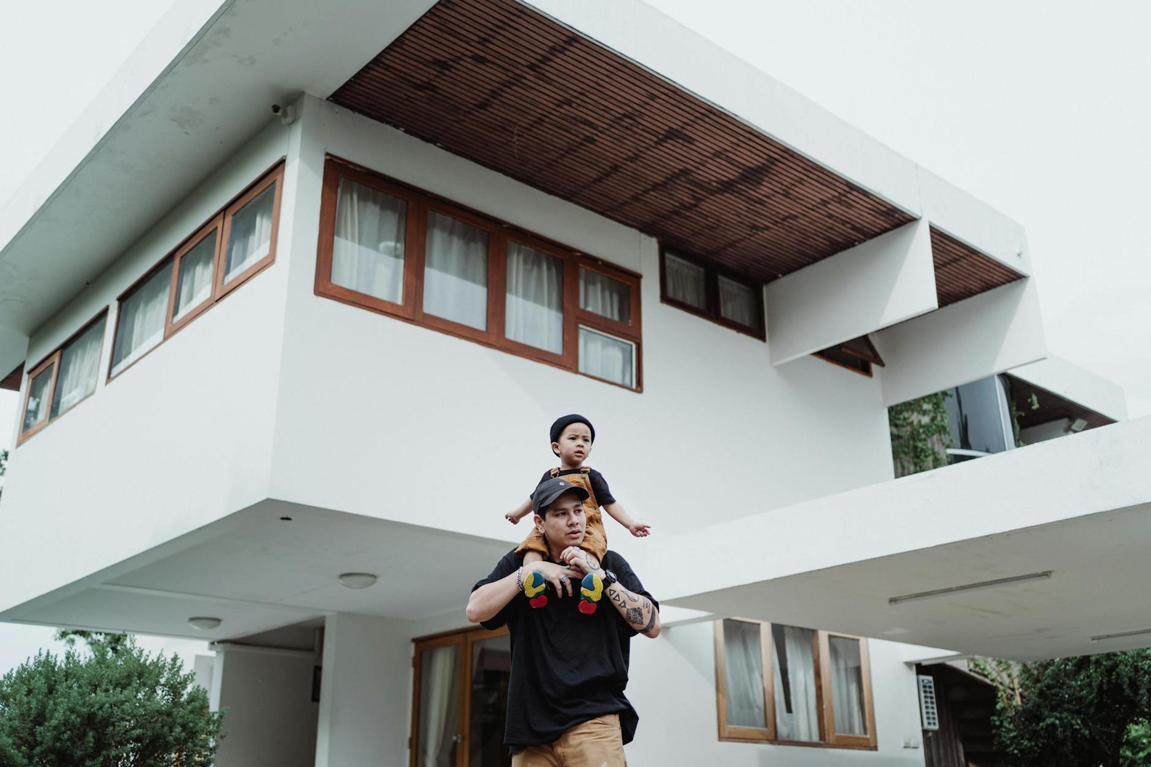 Father and son bonding on a piggyback ride in front of a modern house with unique architecture.