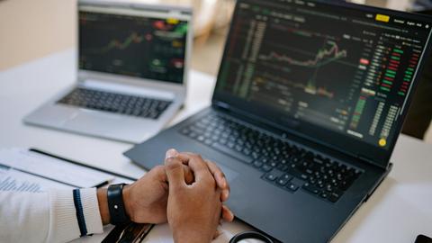 Man seated at a desk using laptops to monitor stock market trends and investments.
