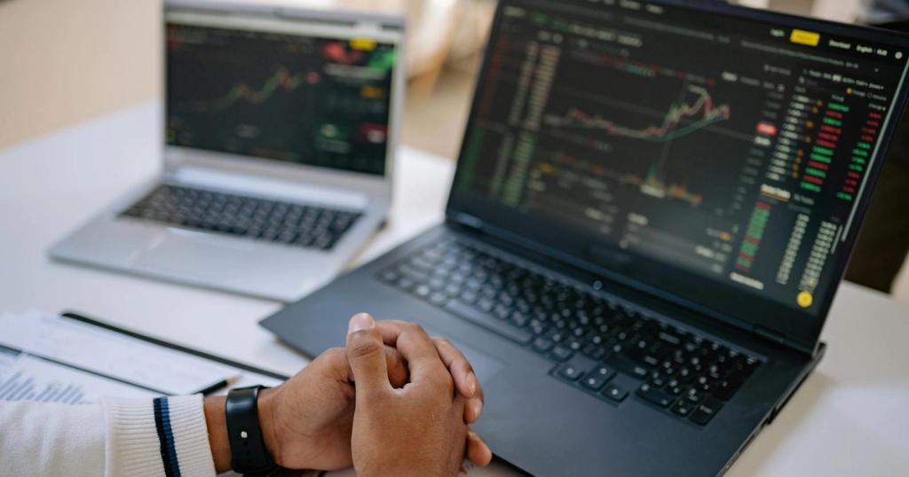 Man seated at a desk using laptops to monitor stock market trends and investments.