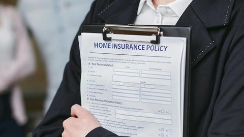 Close-up of a person holding a home insurance policy on a clipboard, captured indoors.
