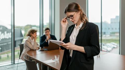 Confident woman reviewing notes leading a business meeting in a modern office setting.