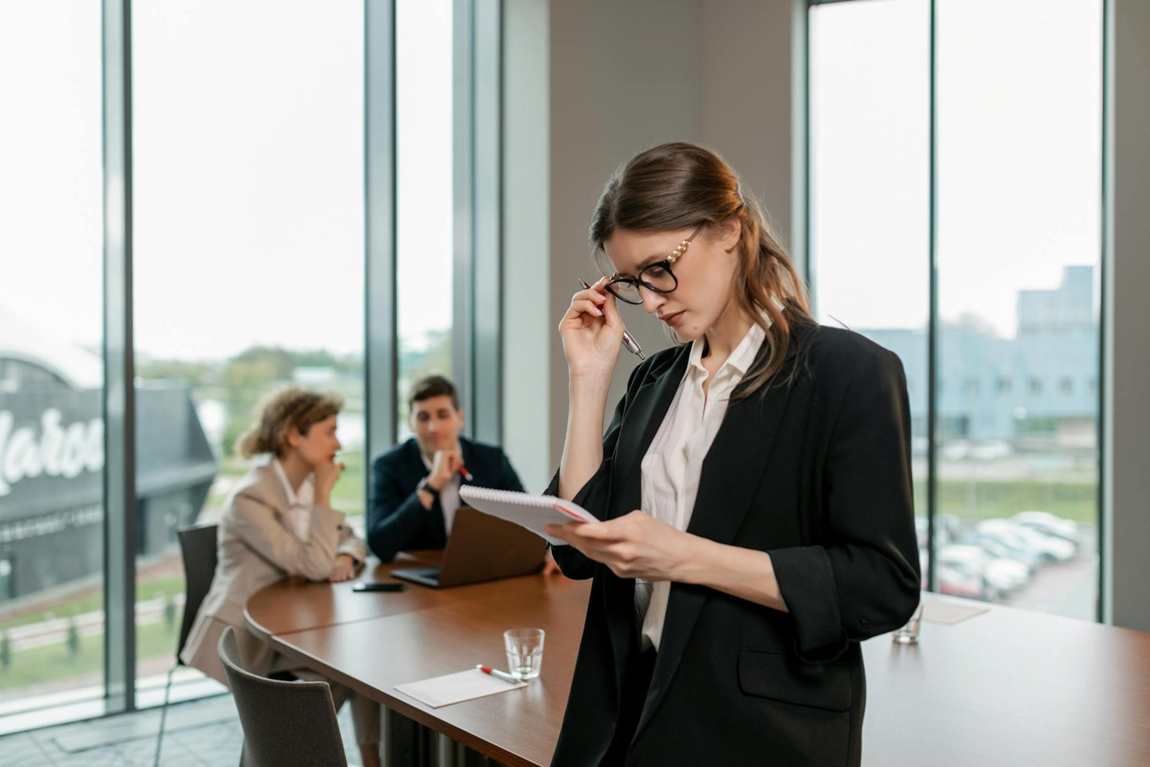 Confident woman reviewing notes leading a business meeting in a modern office setting.