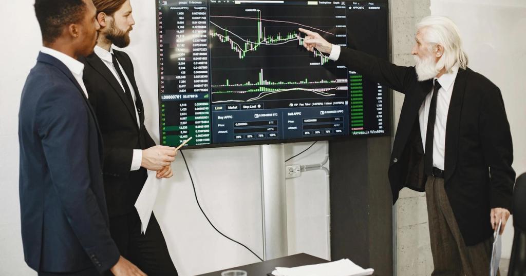 A diverse business team in a meeting analyzing stock market data on a screen.