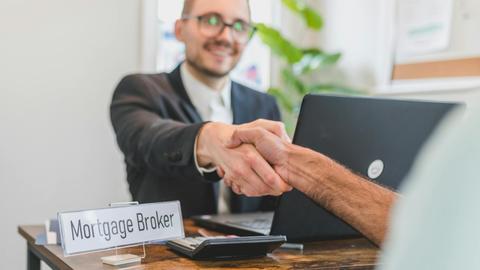 Mortgage broker and client sealing a deal with a handshake in a bright, modern office.