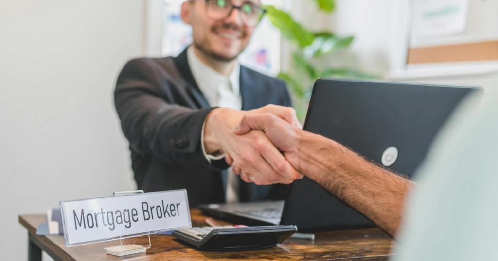 Mortgage broker and client sealing a deal with a handshake in a bright, modern office.