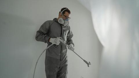 Person in protective gear painting a wall, showcasing house renovation work.