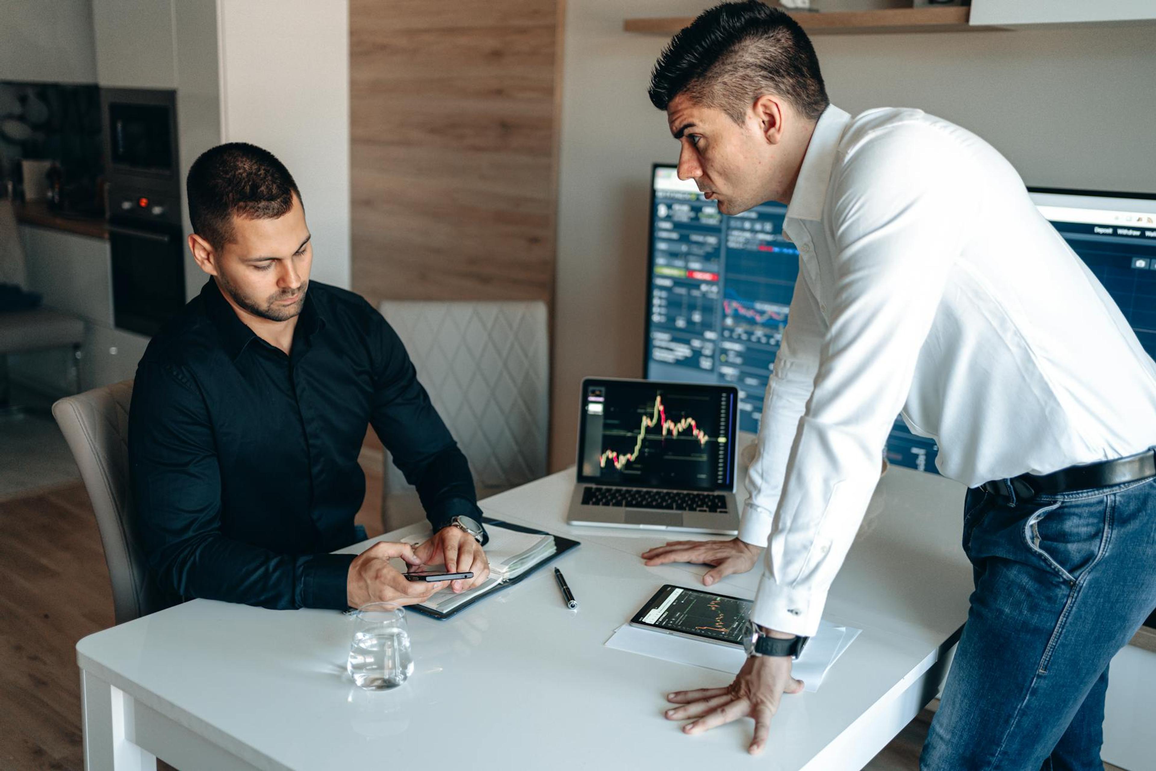Two businessmen discussing digital market trends with laptops and tablets in a modern office.