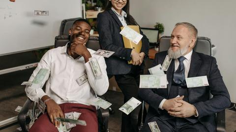 Office scene of diverse business professionals with money scattered, creating a playful environment.