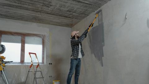 A man painting an interior wall with a roller during a home renovation project.