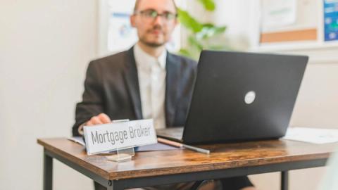 A mortgage broker working at a desk with a laptop in an office setting.