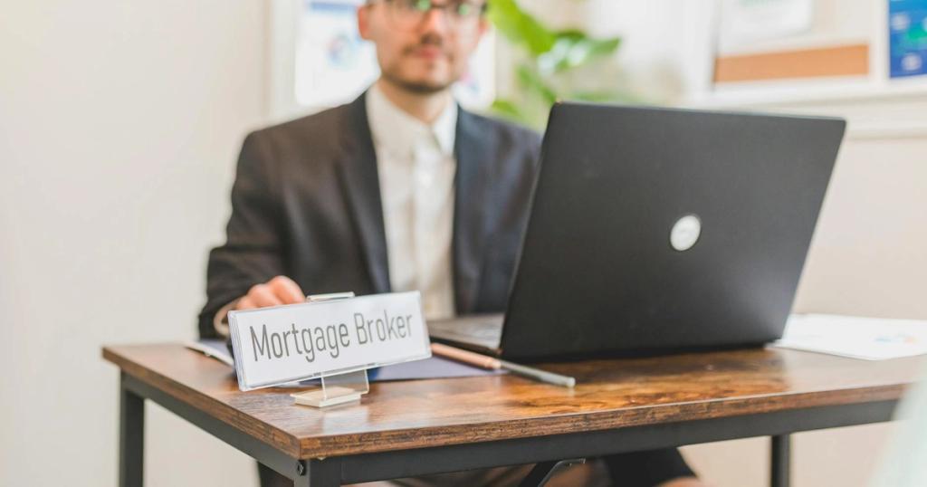 A mortgage broker working at a desk with a laptop in an office setting.