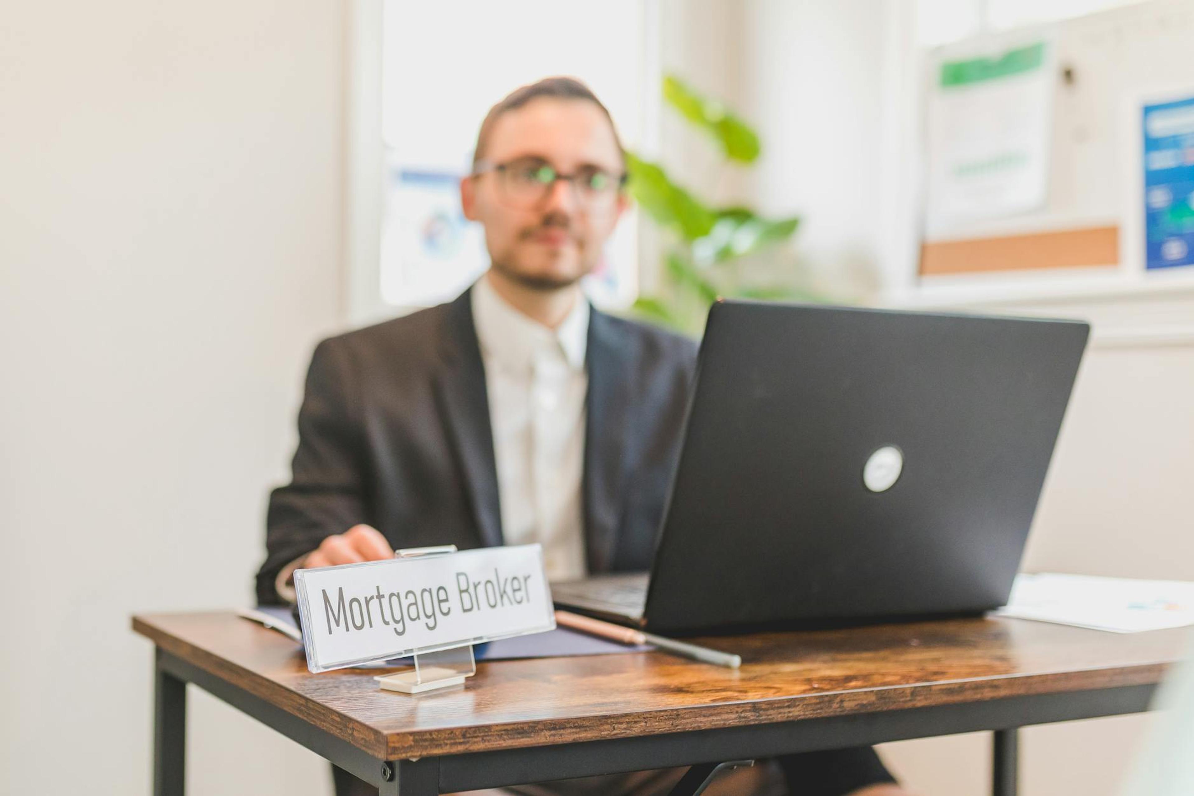 A mortgage broker working at a desk with a laptop in an office setting.