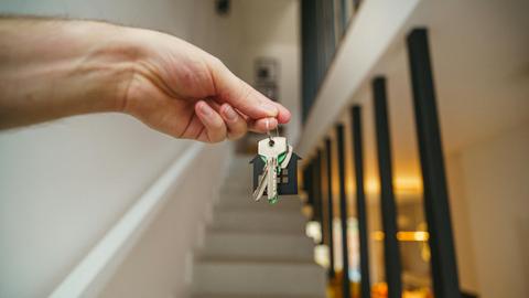 A hand holding house keys in a modern interior, symbolizing new home ownership or real estate investment.