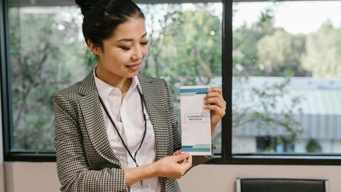 Young professional woman holding a conference program brochure indoors.