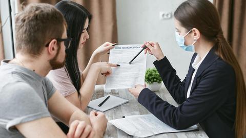 Three adults discuss a home insurance policy at a meeting table indoors.