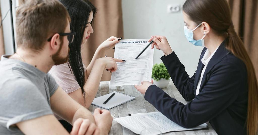 Three adults discuss a home insurance policy at a meeting table indoors.