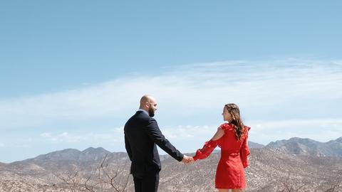 man in black suit jacket holding woman in red dress on top of mountain during daytime