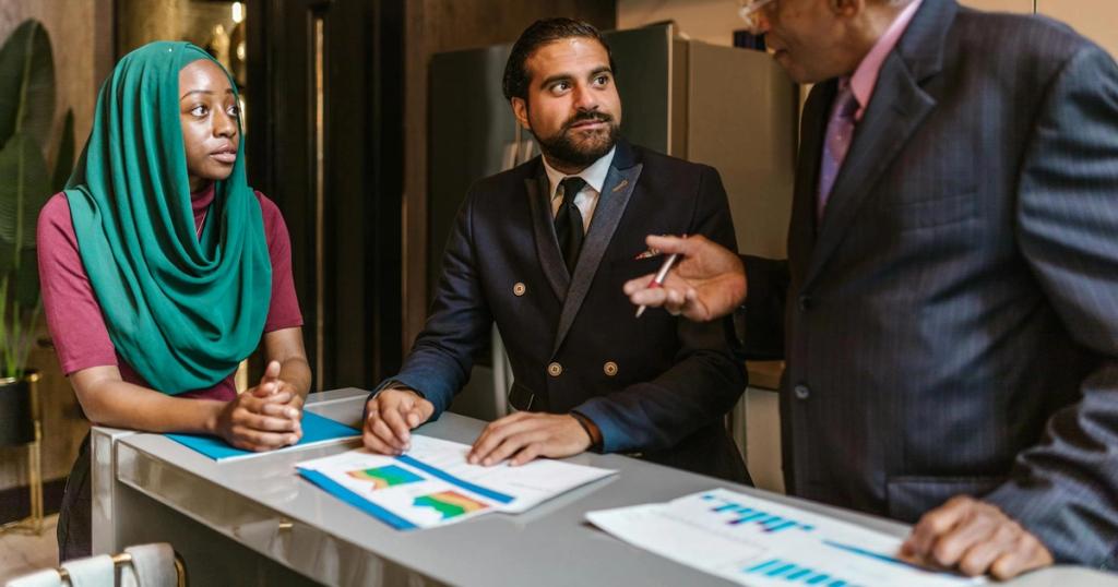 Three business professionals engage in a discussion, showcasing diversity and teamwork in a modern office setting.