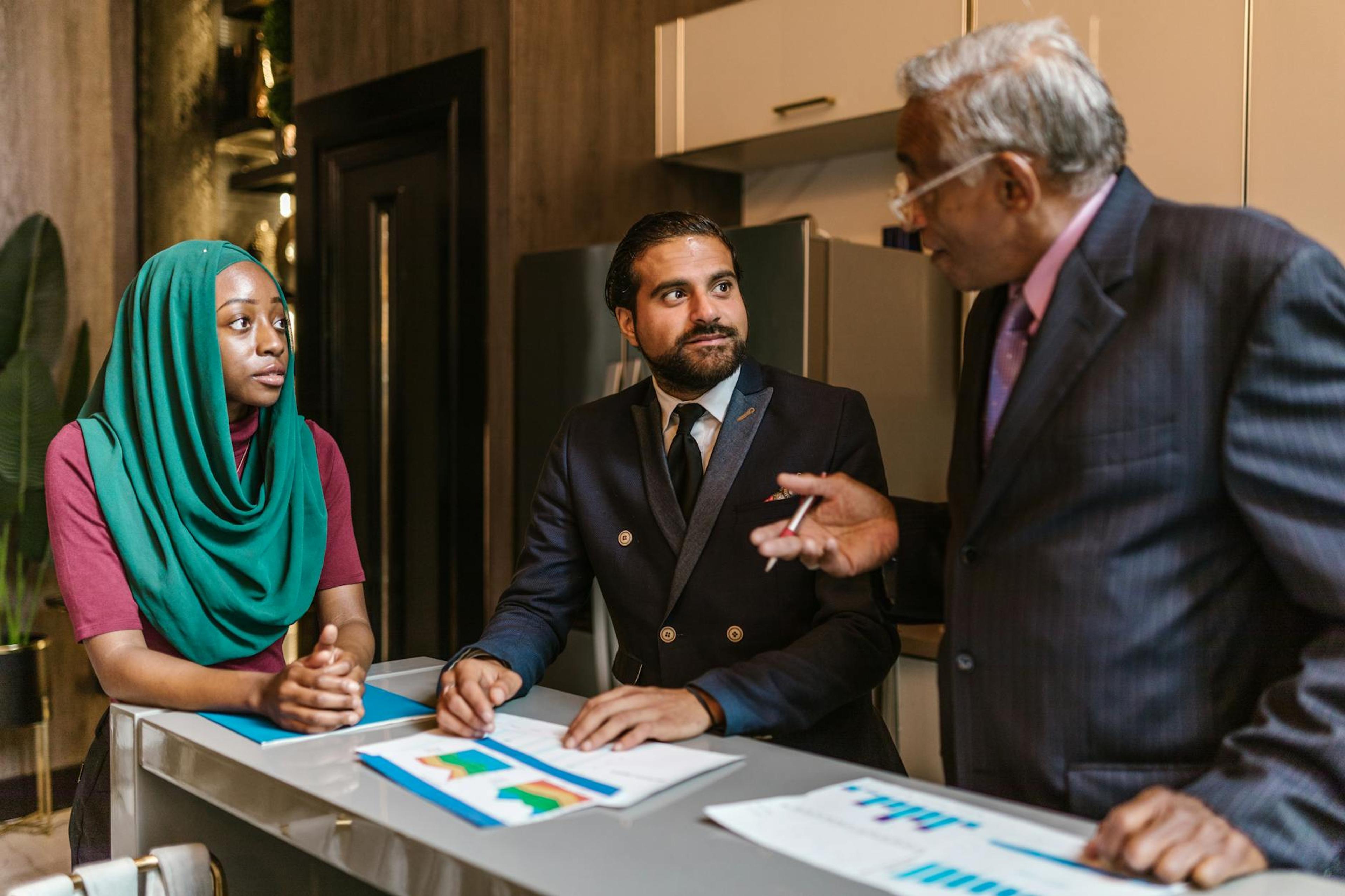Three business professionals engage in a discussion, showcasing diversity and teamwork in a modern office setting.