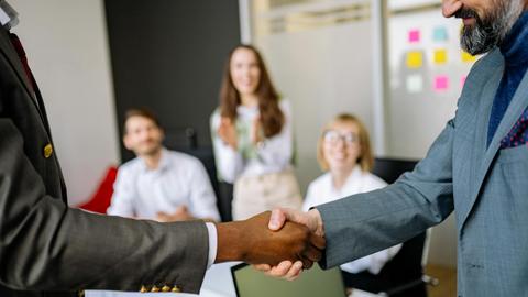 Close-up of a handshake between colleagues in a professional office setting, emphasizing teamwork and agreement.