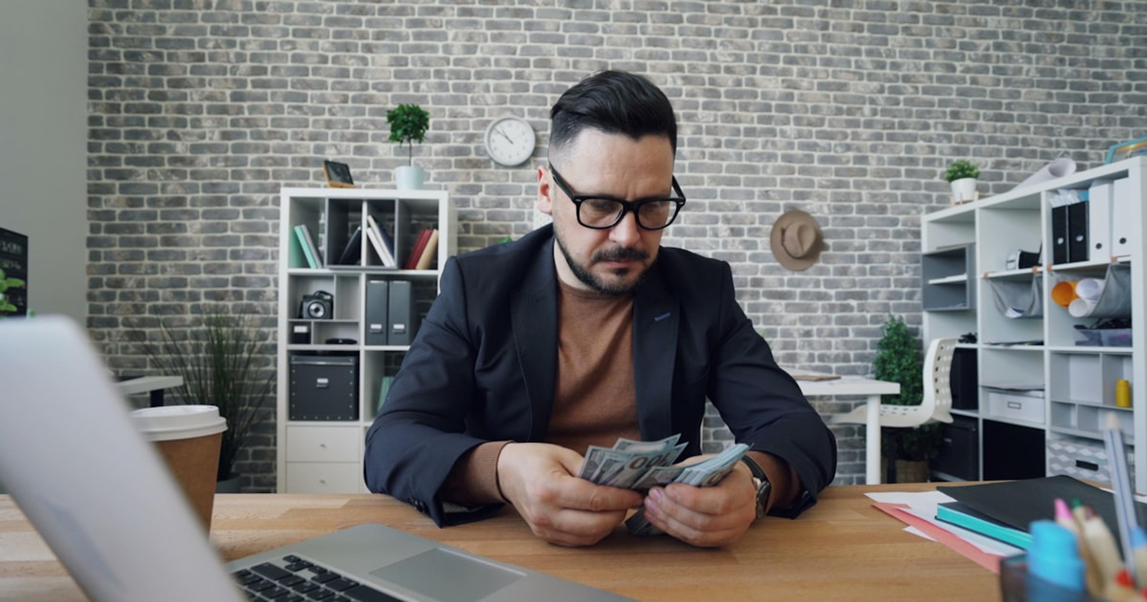 a man sitting at a table with a laptop and money