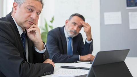Two senior businessmen in suits during a formal meeting in an office setting in Portugal.