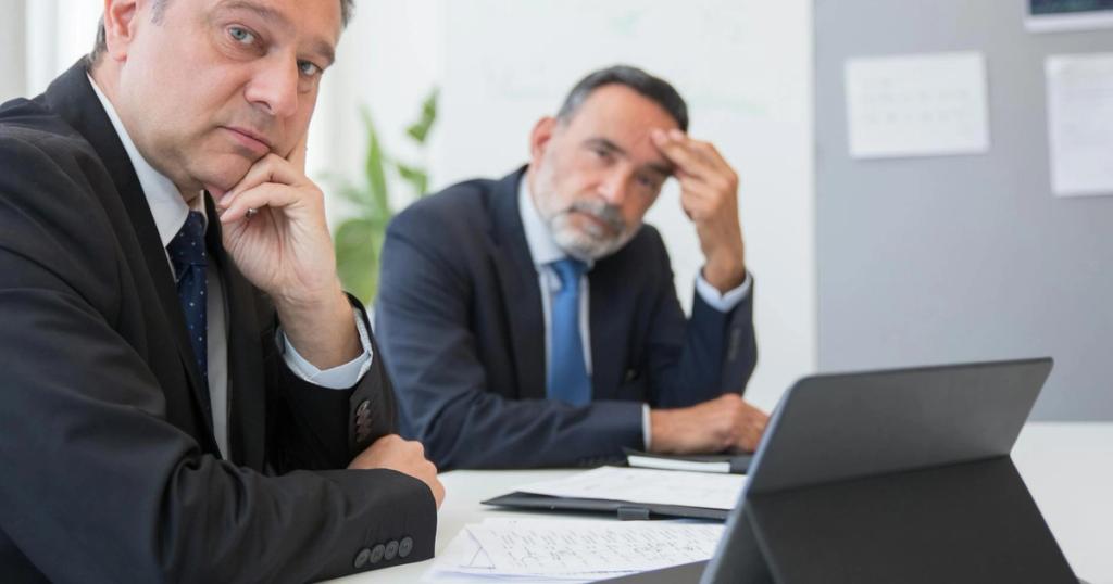 Two senior businessmen in suits during a formal meeting in an office setting in Portugal.