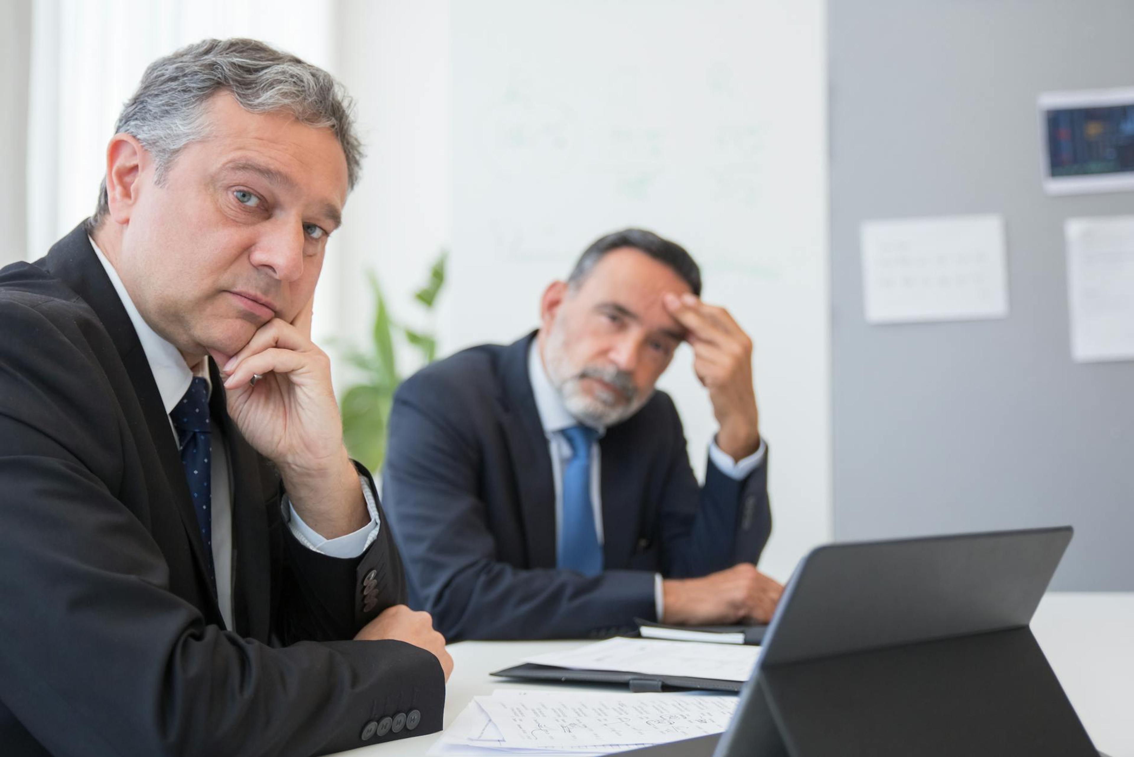 Two senior businessmen in suits during a formal meeting in an office setting in Portugal.
