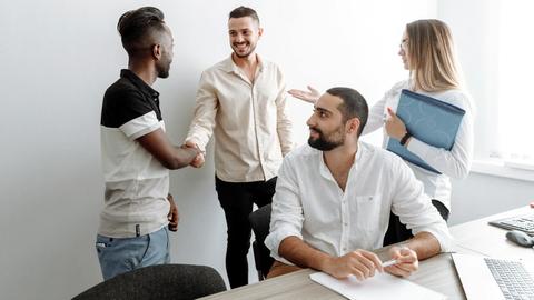 A team of diverse professionals shaking hands and smiling in an office setting, symbolizing cooperation.