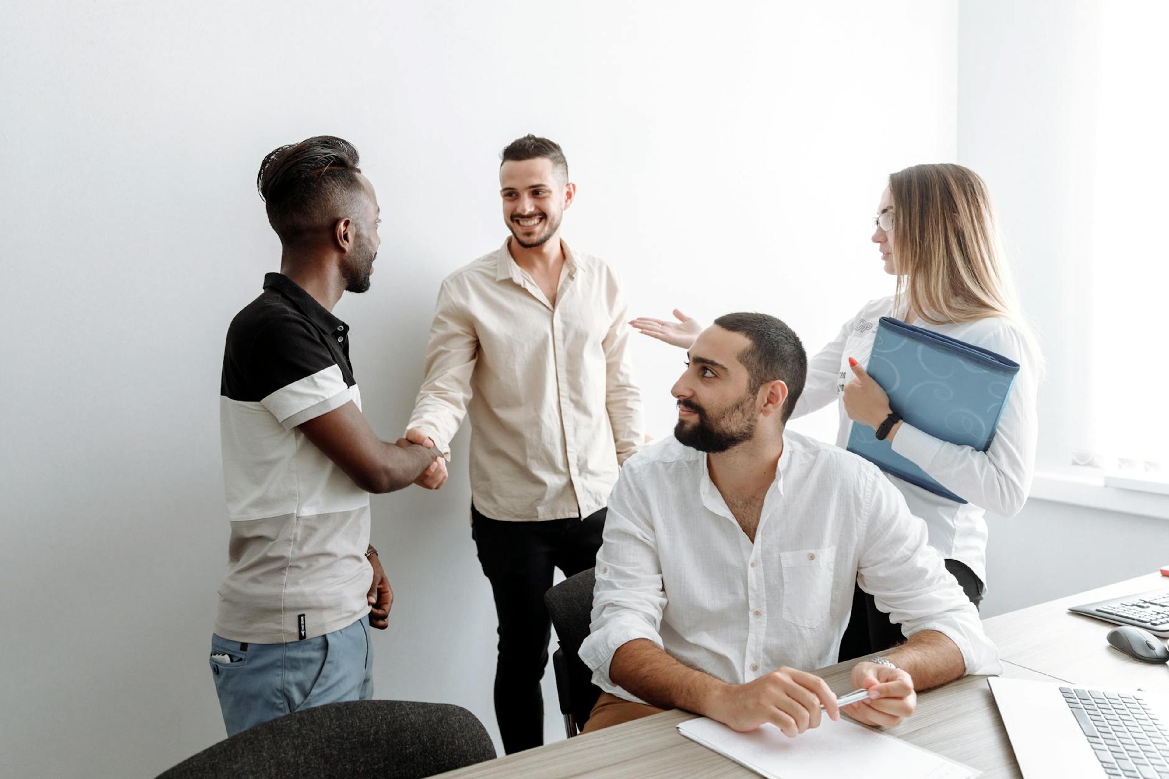 A team of diverse professionals shaking hands and smiling in an office setting, symbolizing cooperation.