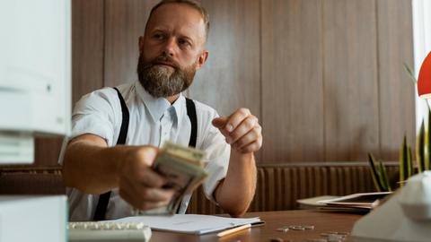 Businessman in a corporate office handling a stack of cash at his desk.