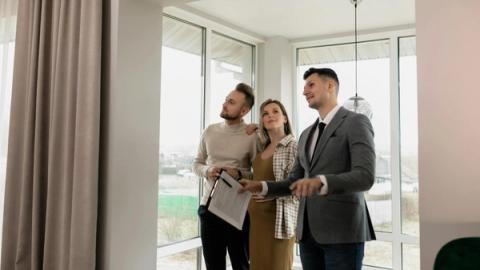 A real estate agent showing a modern home to a young couple during a daytime viewing.