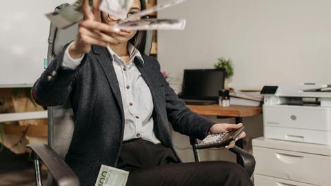A businesswoman in a suit throws money while calculating finances in a modern office.