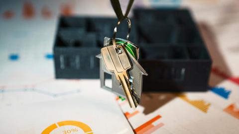 Real estate keys on house keychain with financial graphs, symbolizing property investment.