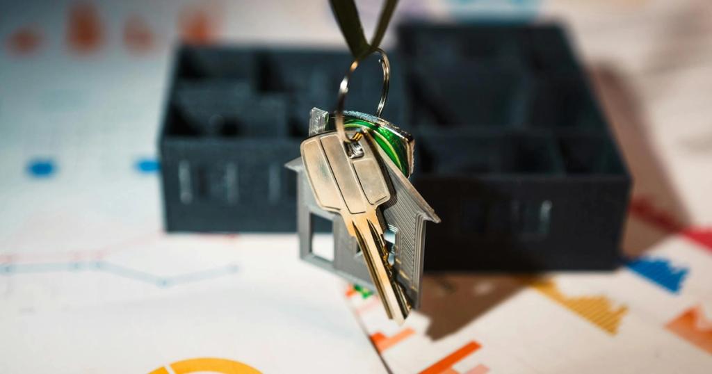 Real estate keys on house keychain with financial graphs, symbolizing property investment.
