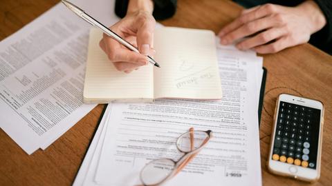 Close-up of a person writing in a notebook with documents and a calculator, managing finances.