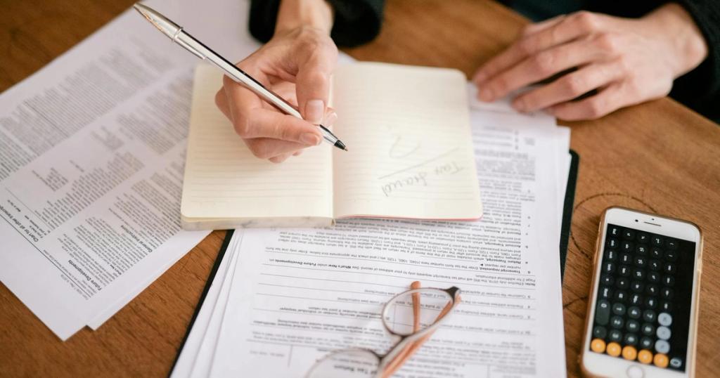 Close-up of a person writing in a notebook with documents and a calculator, managing finances.