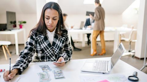 Businesswoman calculating finances with cash and a laptop in a modern office.