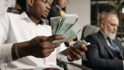 Three professionals in business attire counting cash in a modern office setting.