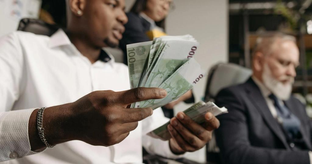 Three professionals in business attire counting cash in a modern office setting.